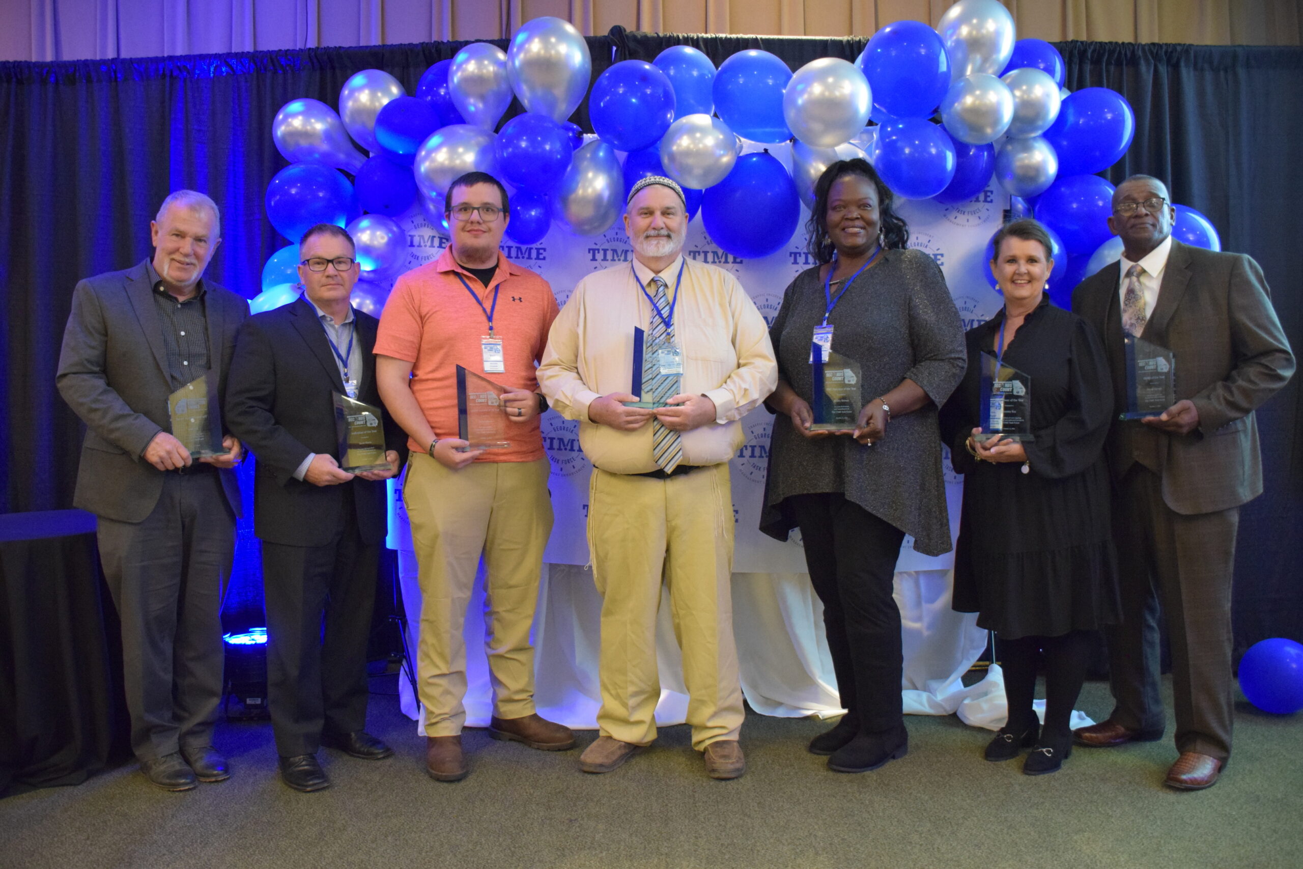 The seven TIM Annual Award Winners pose with their awards and the 2024 Awards Banquet, which took place during the 2024 conference.