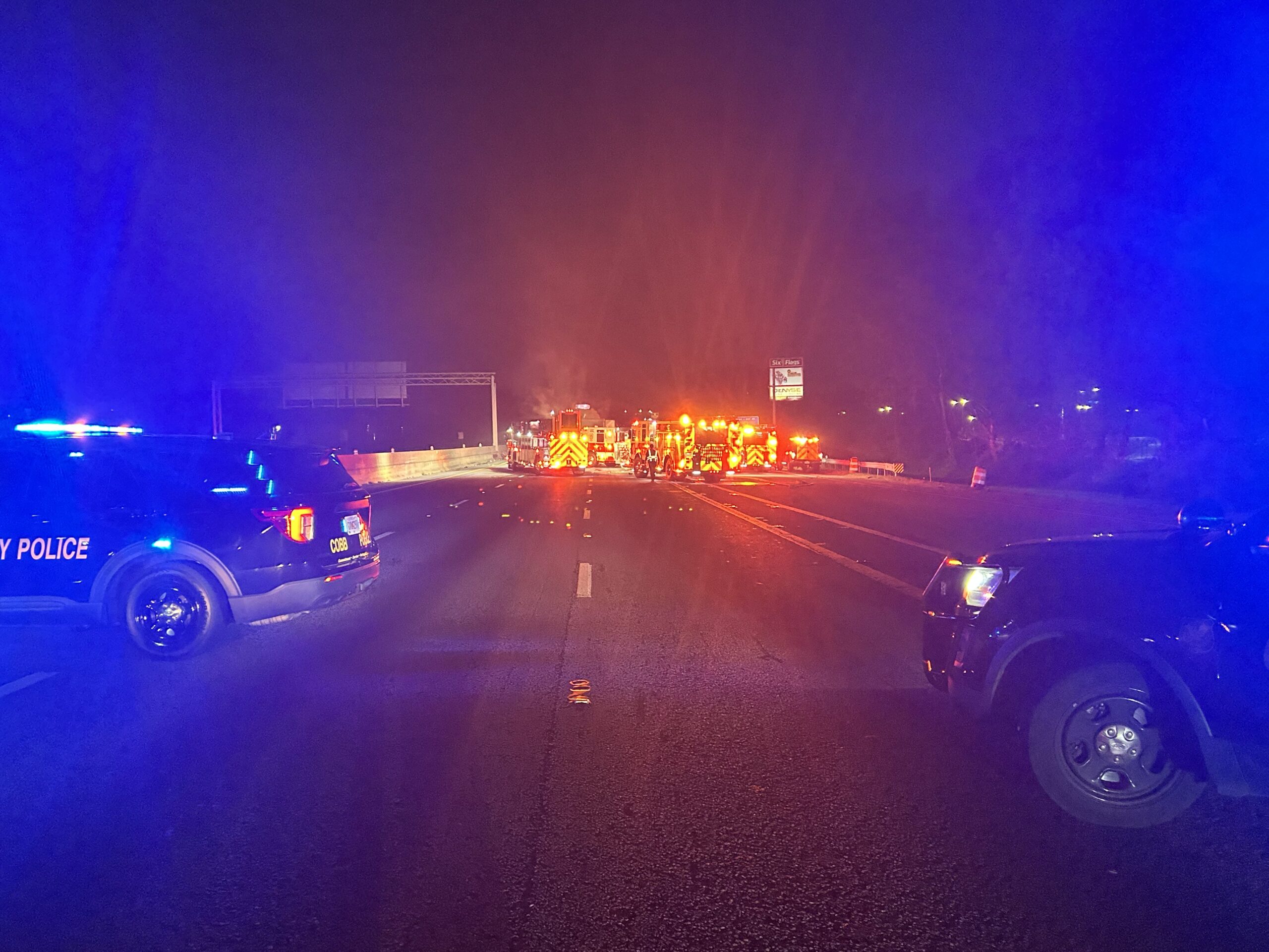 A nighttime incident scene on the road with two police cars up close with their blue lights on, and fire trucks with their red lights on in the distance. 