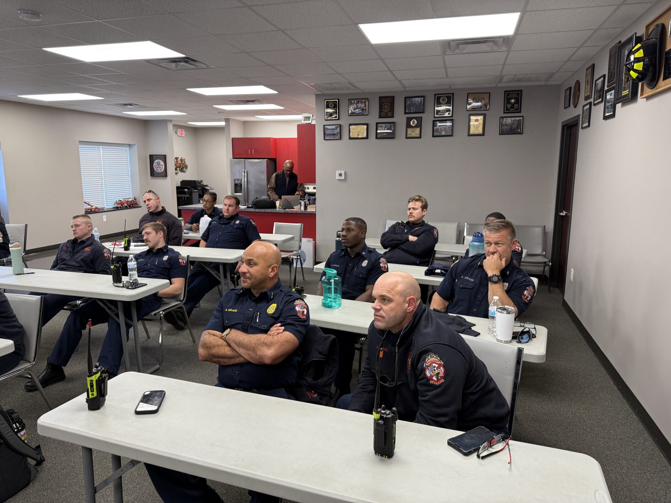 Firefighter trainees in a room at rows of tables with their attention fixed on the space in front of them, presumably on the instructor and class content.